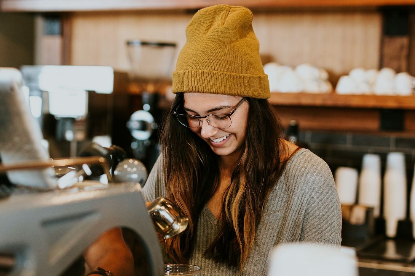 Barista mit Wollmütze bereitet hinter dem Tresen einen Kaffee zu